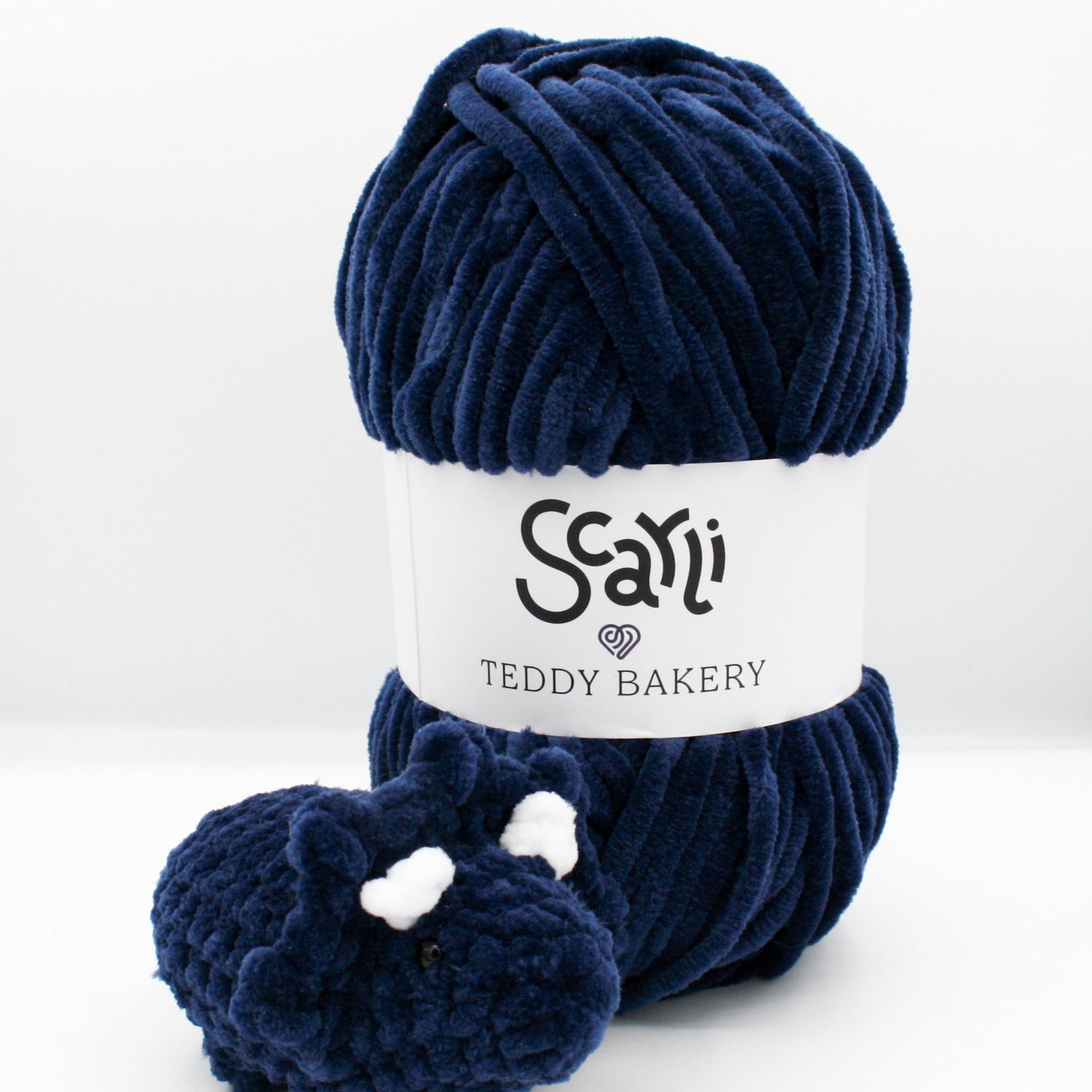 skein of navy blue chenille plush yarn and amigurumi crochet triceratops plushie