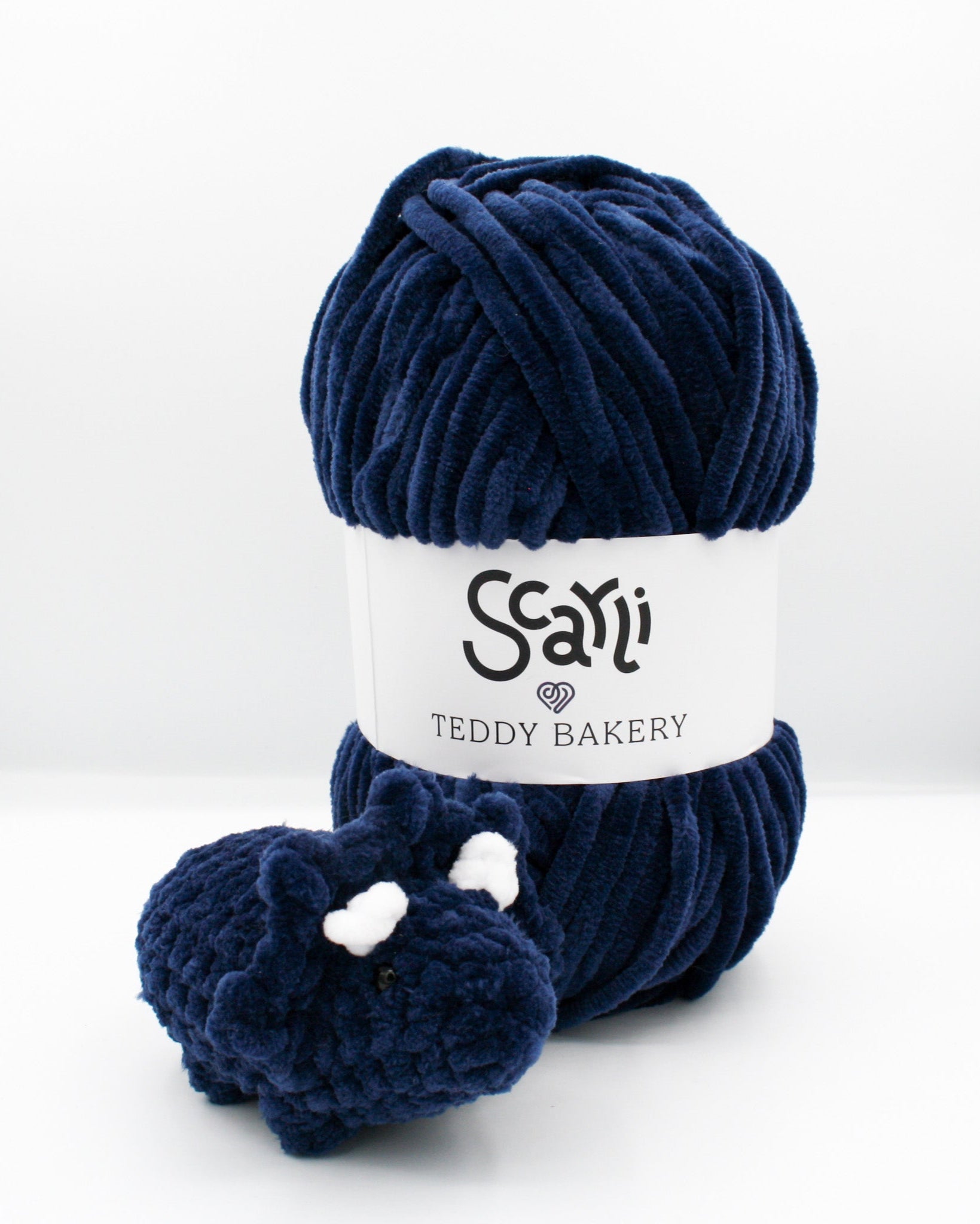 skein of navy blue chenille plush yarn and amigurumi crochet triceratops plushie