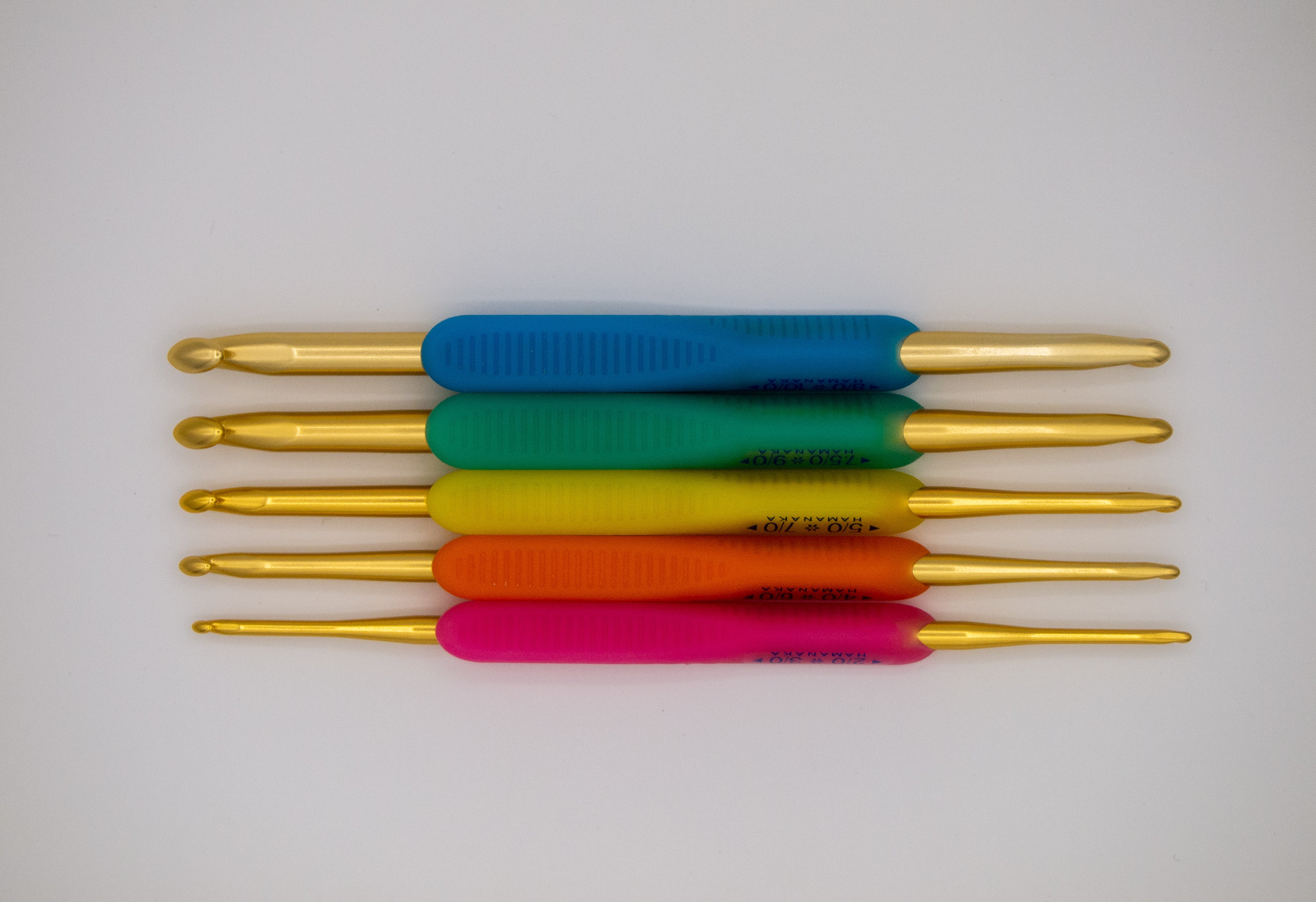 Hamanaka crochet hook set. Includes five hooks with 10 hook sizes including 2mm, 2.2mm, 2.5mm, 3mm, 3.5mm, 4mm, 4.5mm, 5mm, 5.5mm, 6mm. Gold aluminium hook with plastic ergonomic handle in blue, green, yellow, orange and pink